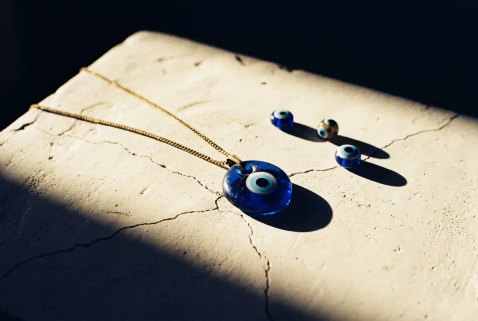 Cobalt blue glass evil eye pendant on cracked pale plaster with three smaller nazar beads
