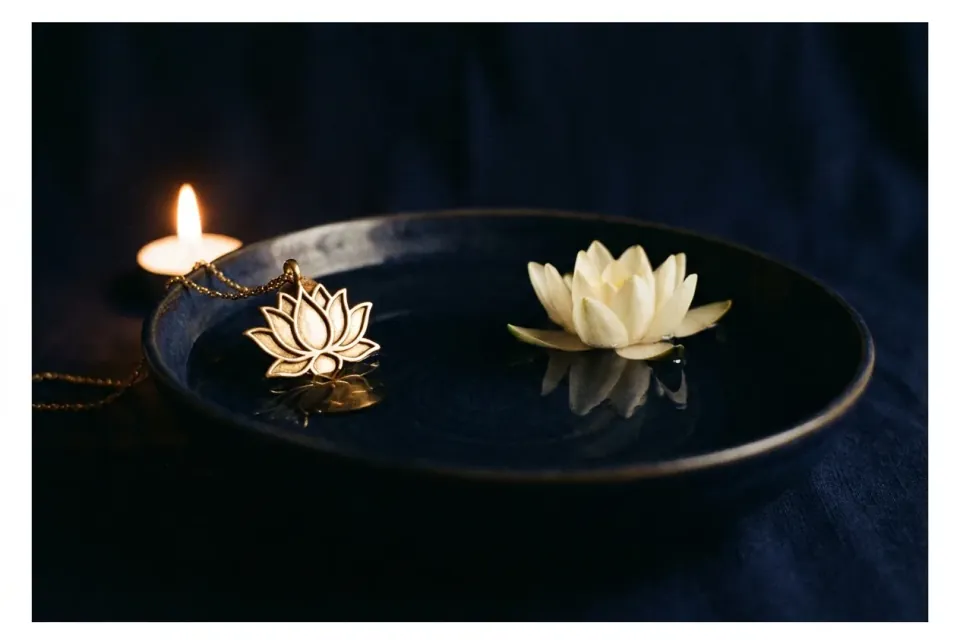 Gold lotus pendant beside a black bowl of still water holding a floating white lotus