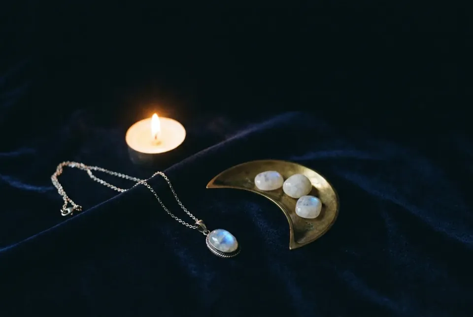 Rainbow moonstone pendant with blue sheen on ink-blue velvet beside a brass crescent dish