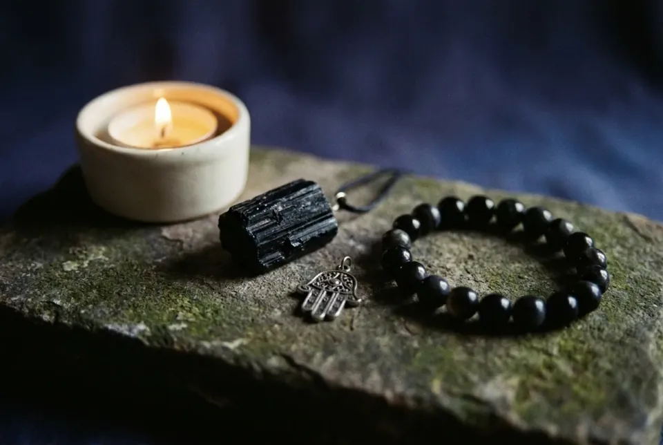 Black tourmaline pendant, silver hamsa and obsidian bracelet arranged around a tealight